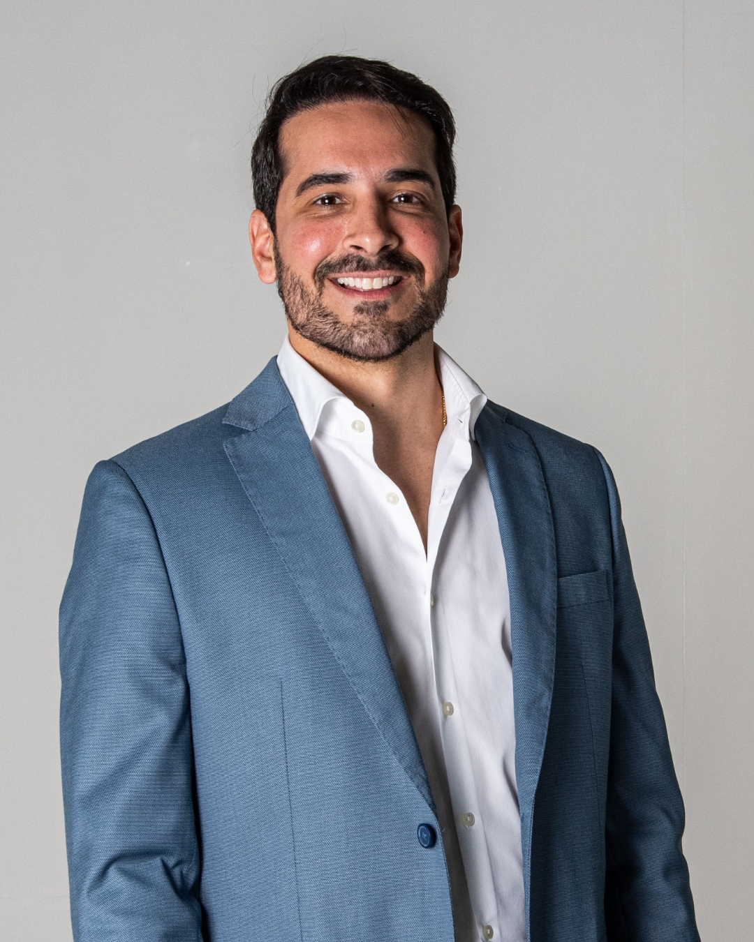 Lucas Abreu, retrato em traje azul sobre fundo claro, sorrindo.